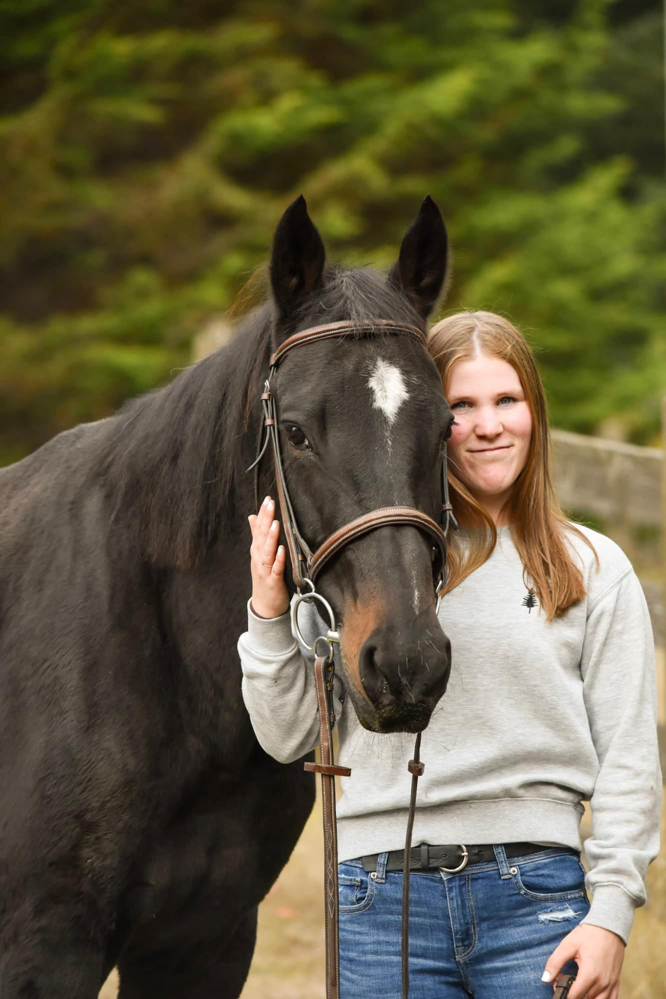 Smiling rider resting her cheek against her dark bay horse